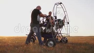 汽车滑翔伞在日落时分用一个木制螺旋桨站在田野里，两名飞行员在飞行前为发动机预热